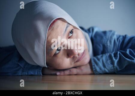 Triste asiatique musulmane femme posant la tête sur la table et regardant avec le vide stum pensant à quelque chose, dans la pièce sombre Banque D'Images