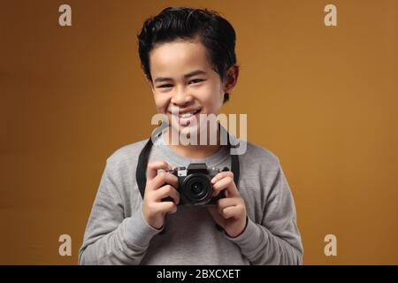 Joyeux garçon asiatique faisant des activités de loisirs de photographie, enfant comme photographe prenant des photos avec son appareil photo numérique, sur fond jaune Banque D'Images