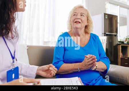 Femme âgée qui parle à un médecin qui lui rend visite à la maison et qui écrit une ordonnance Banque D'Images