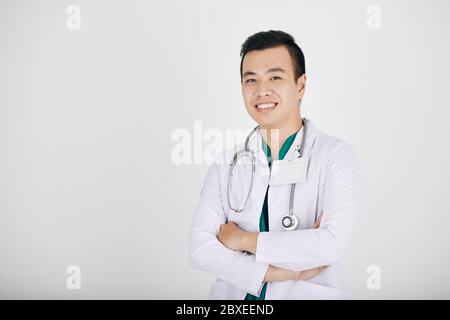 Portrait de la thérapie souriant jeune docteur vietnamien croisant les bras et regardant la caméra, isolé sur shite Banque D'Images