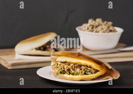 Le hamburger chinois Roujiamo est un plat populaire de rue. Sur la photo, un sandwich fait maison est présenté dans une assiette blanche sur une table en bois noir. Banque D'Images