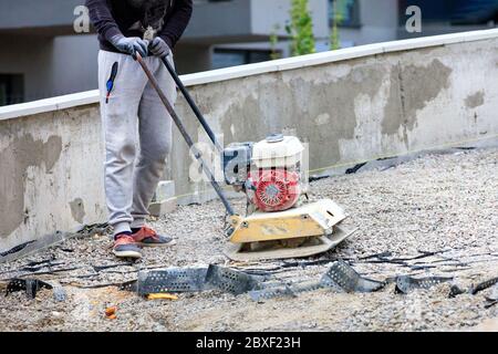 Un employé de l'entretien routier utilise une plaque à essence compactant la pierre concassée sur un chantier de réparation. Banque D'Images