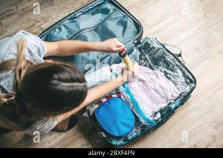 Une fille emboîte des objets ou des vêtements avec une pompe à vide pour gagner de la place dans une valise de voyage. Banque D'Images