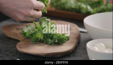 homme déchirant les feuilles de chou frisé pour les rendre plus tendres pour la salade vue latérale sur la cuisine Banque D'Images