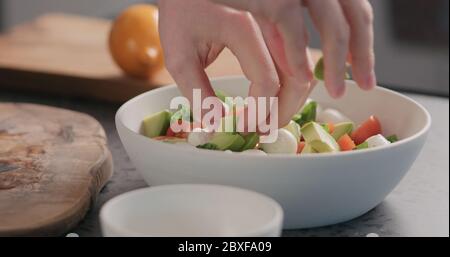 l'homme ajoute l'avocat dans la salade avec le chou vert, la mozzarella et les tomates dans un bol blanc sur le comptoir de la cuisine Banque D'Images