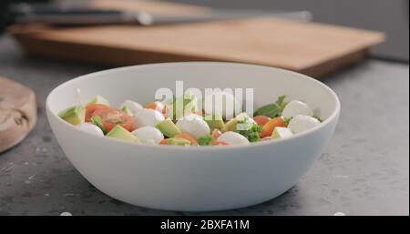 presser le citron orange dans la salade avec le chou vert, l'avocat, la mozzarella et les tomates dans un bol blanc sur le comptoir de la cuisine Banque D'Images