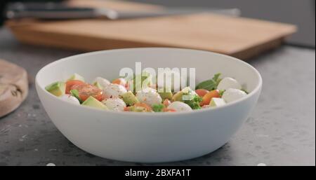 ajouter les épices dans la salade avec le chou vert, l'avocat, la mozzarella et les tomates dans un bol blanc sur le comptoir de la cuisine Banque D'Images