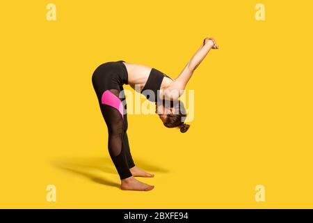 Une fille sportive avec un petit pain dans un vêtement de sport serré faisant du sport, se pliant et étirant les mains vers l'arrière, réchauffant les muscles d'entraînement pour plus de flexibilité. Plein Banque D'Images