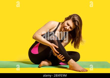 La Sportswoman criant de douleur dans la jambe, assis sur le tapis de gym touchant le caviar blessé, souffrant de la tension musculaire de mollet après l'entraînement de yoga, de mal à déplacer sp Banque D'Images