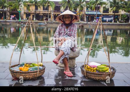 HOI AN, VIETNAM - 27 MARS 2017 : une dame âgée qui attend à côté de la rivière à Hoi une vente de fruits. Banque D'Images