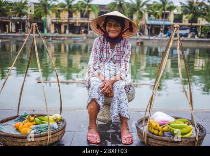 HOI AN, VIETNAM - 27 MARS 2017 : une dame âgée qui attend à côté de la rivière à Hoi une vente de fruits. Banque D'Images