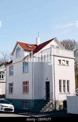 La façade d'une maison rectangulaire blanche avec un toit rouge, une voiture blanche disséquée le long de la route à Reykjavik, la capitale de l'Islande. Banque D'Images