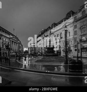 Un touriste solitaire passe à travers une bande de lumière dans un cirque sombre de Piccadilly à Londres pendant le confinement alors que la pandémie de coronavirus balaye le monde. Banque D'Images