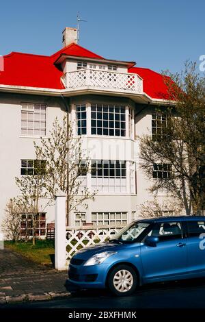 Maison de trois étages avec grandes fenêtres panoramiques et plancher de grenier avec toit rouge à Reykjavik, la capitale de l'Islande. Une voiture bleue est garée près de Banque D'Images