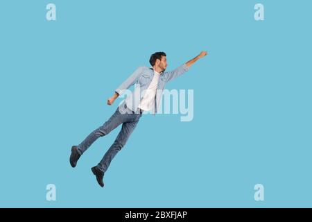 Portrait complet d'un homme en tenue denim volant en tant que super-héros avec la main levée et inspiré l'expression ambitieuse, atteindre le but, sauter haut dans Banque D'Images