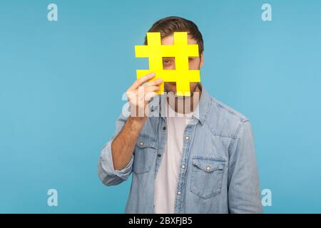 Portrait d'un homme en chemise denim, à travers le grand symbole hashtag jaune, debout isolé sur fond bleu avec espace pour le texte marqué, pop Banque D'Images