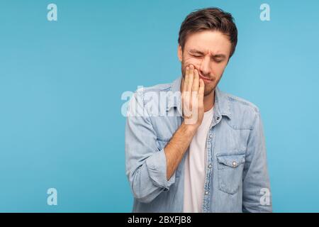 Problèmes dentaires. Portrait d'un homme malsain dans une chemise en denim appuyant sur la joue, souffrant de maux de dents aigus, de maladies parodontales, de cavités ou de douleurs à la mâchoire Banque D'Images