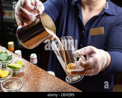 Le barman se tient derrière le bar et verse une boisson de café d'une cafetière en acier inoxydable dans un grand gobelet en verre Banque D'Images