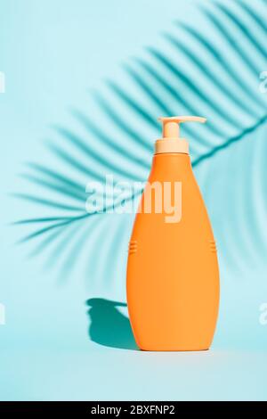 Contenant orange pour lotion sans étiquette sur fond bleu avec feuille de fougères Banque D'Images