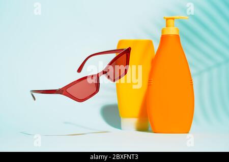 Contenants orange sans étiquette pour lotion, lunettes de soleil sur fond bleu, espace pour le texte Banque D'Images