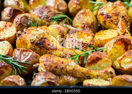 Cuisses de poulet chaudes cuites avec pommes de terre épicées sur plaque de cuisson sur fond noir Banque D'Images