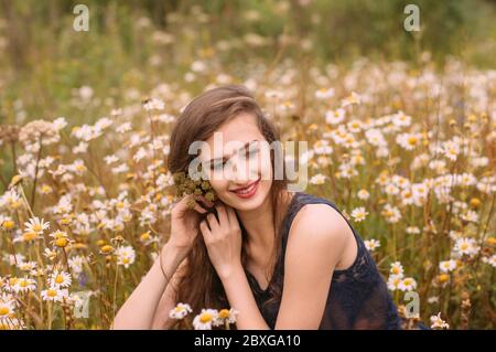 Jeune belle fille avec des fleurs dans les cheveux dans le champ de camomille en été Banque D'Images