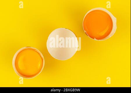 Jaunes d'œufs crus dans les moitiés de coquilles d'œufs brunes fissurées sur fond jaune. Ligne diagonale Banque D'Images
