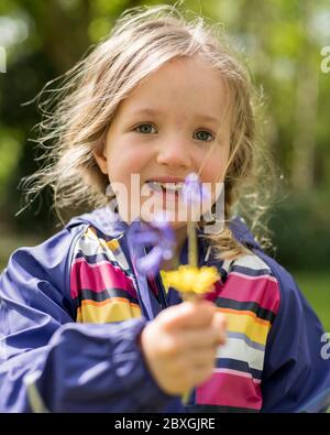 fille de 4 ans planter et jardiner, planter des plantes de concombre, porter un manteau de pluie orange/violet, jour ensoleillé, aide pré-école dans le jardin Banque D'Images