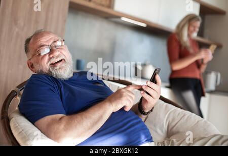 homme âgé avec un smartphone assis dans une chaise à domicile. Banque D'Images