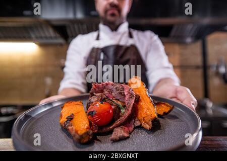 Gros plan du chef montrant de la viande rôtie avec des patates douces et des tomates sur l'assiette Banque D'Images