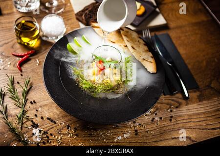 Ceviche de pétoncle à la mangue, au piment et à la coriandre servie dans une assiette avec de la fumée de glace liquide. Délicieux aliments sains servis pour le déjeuner sur une table Banque D'Images