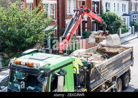 Un homme travaillant dans une veste haute visibilité et un casque de sécurité contrôlant la saisie sur un camion plein de terre, Londres, Royaume-Uni Banque D'Images