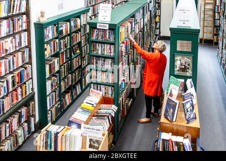 Une femme en manteau rouge parcourant les étagères de la bibliothèque ai, Londres, Royaume-Uni Banque D'Images