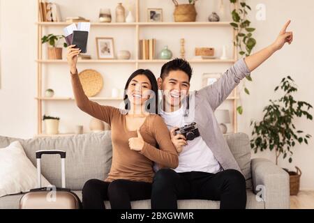 Couple tenant des billets et des passeports faisant des gestes de Thumbs-Up assis sur le canapé Banque D'Images