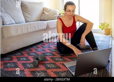 Jolie fille espagnole pratique en ligne gymnastique à la maison dans le salon et faire une pause Banque D'Images