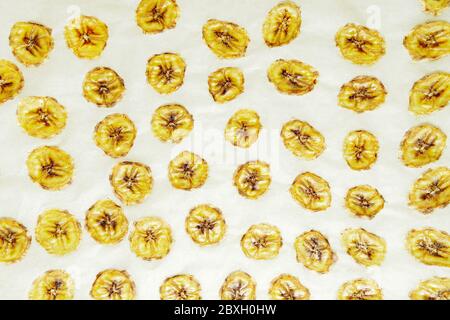 Chips de banane, tranches de bananes mûres fraîches comme fond de nourriture. Cuisson sur papier parchemin à la maison Banque D'Images