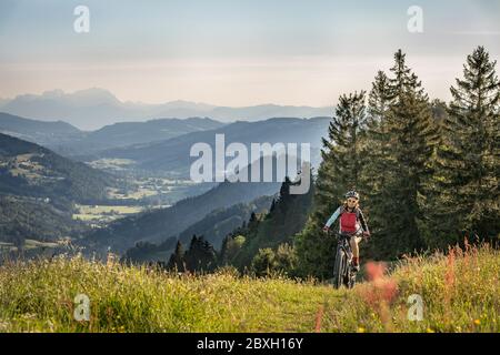 Jolie femme âgée qui monte sur son vélo électrique au-dessus d'Oberstaufen avec une vue spectaculaire sur la vallée de Bregenz, les Alpes d'Allgau, la Bavière en Allemagne Banque D'Images