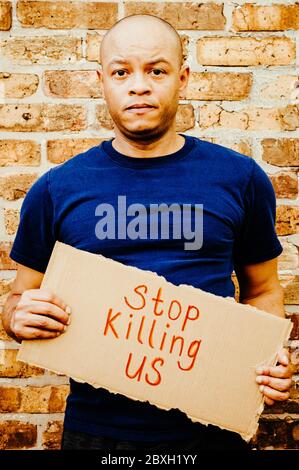 Un homme noir porte un panneau qui dit « Stop nous tuant » pour protester contre la brutalité policière Banque D'Images