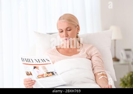 Femme mature lisant le journal dans la chambre d'hôpital Banque D'Images