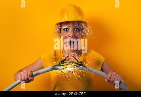 Une fille de travailleur avec un chapeau casse un câble électrique. Fond jaune Banque D'Images