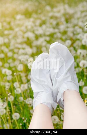 Masque hydratant pour les pieds à talons secs. Femme portant une fois des chaussettes de masque hydratantes de pied dehors avec pissenlit doux pré sur fond. Banque D'Images