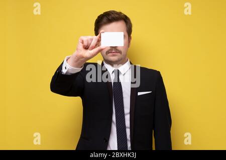 Homme caucasien en costume montrant la carte de visite donnant un geste parfait ou ok. Studio tourné sur un mur jaune. Banque D'Images