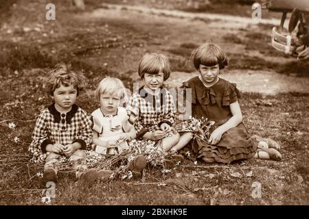 Allemagne - VERS les années 1920 : photo de groupe de quatre petites filles assises sur l'herbe dans le jardin. Archive vintage photographie Art déco Banque D'Images