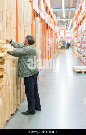 l'homme dans un masque médical de protection dans un magasin de quincaillerie choisit des planches. l'homme est protégé du coronovirus. photo verticale Banque D'Images