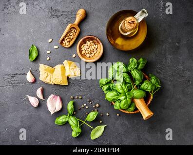 Cuisson de la sauce pesto. Feuilles de basilic, huile d'olive, ail, pignons et parmesan. Vue de dessus sur une table en pierre sombre Banque D'Images