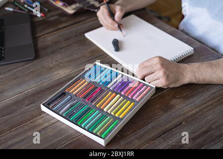 personne peignant avec une craie pastel sur un papier blanc avec une pallette de craies pastel sur la table en bois Banque D'Images