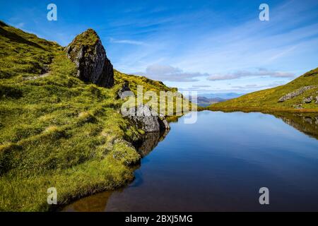 Paysage d'été des Highlands écossais avec un ciel bleu profond et des rochers se reflétant dans un petit étang près du sommet de Meall nan Tarmachan. Banque D'Images