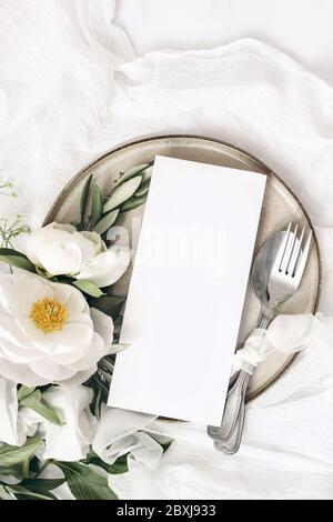 Ambiance festive de mariage d'été. Table en marbre avec couverts, branches d'olive, fleurs de pivoine blanches, assiette en grès et ruban de soie. Restaurant vide Banque D'Images