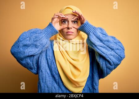 Jeune belle brune musulmane femme portant le hijab arabe sur fond jaune isolé essayant d'ouvrir les yeux avec les doigts, endormi et fatigué pour la mornine Banque D'Images