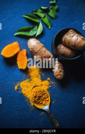 Poudre de curcuma et racine de curcuma sur fond bleu, avec feuilles de curry. Vue de dessus de l'aldi aux épices indiennes. Banque D'Images